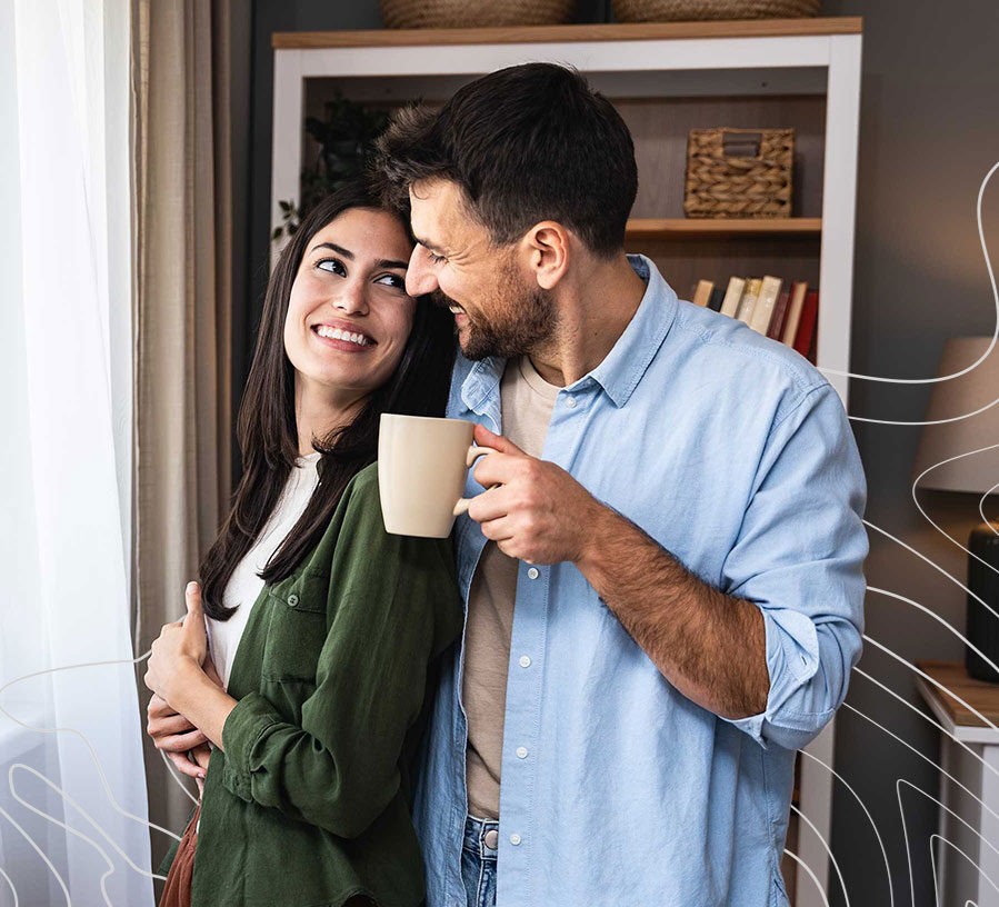 A couple smiles at each other while the man holds a coffee mug