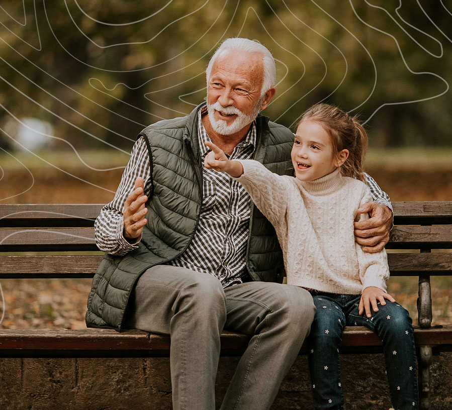 A senior man smiles as his granddaughter points