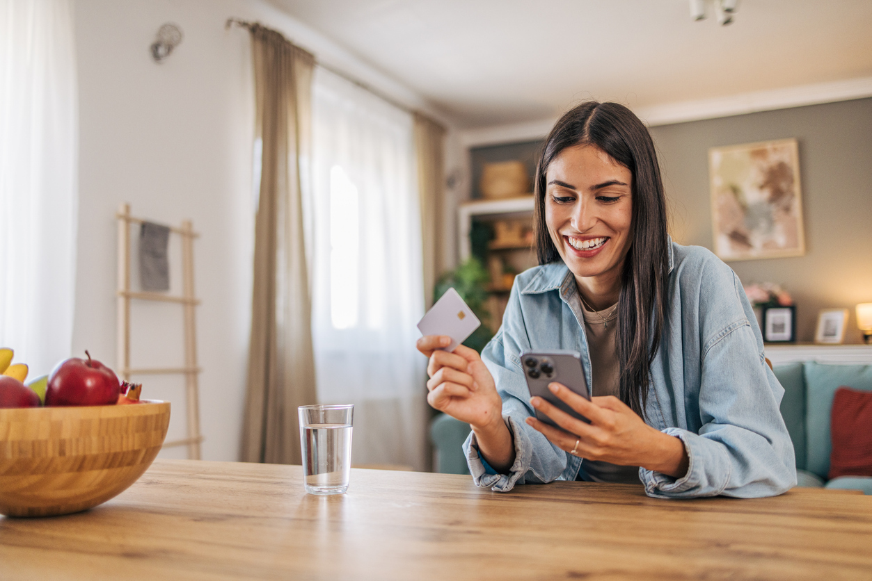 Adult woman looking at her phone with credit card in other hand